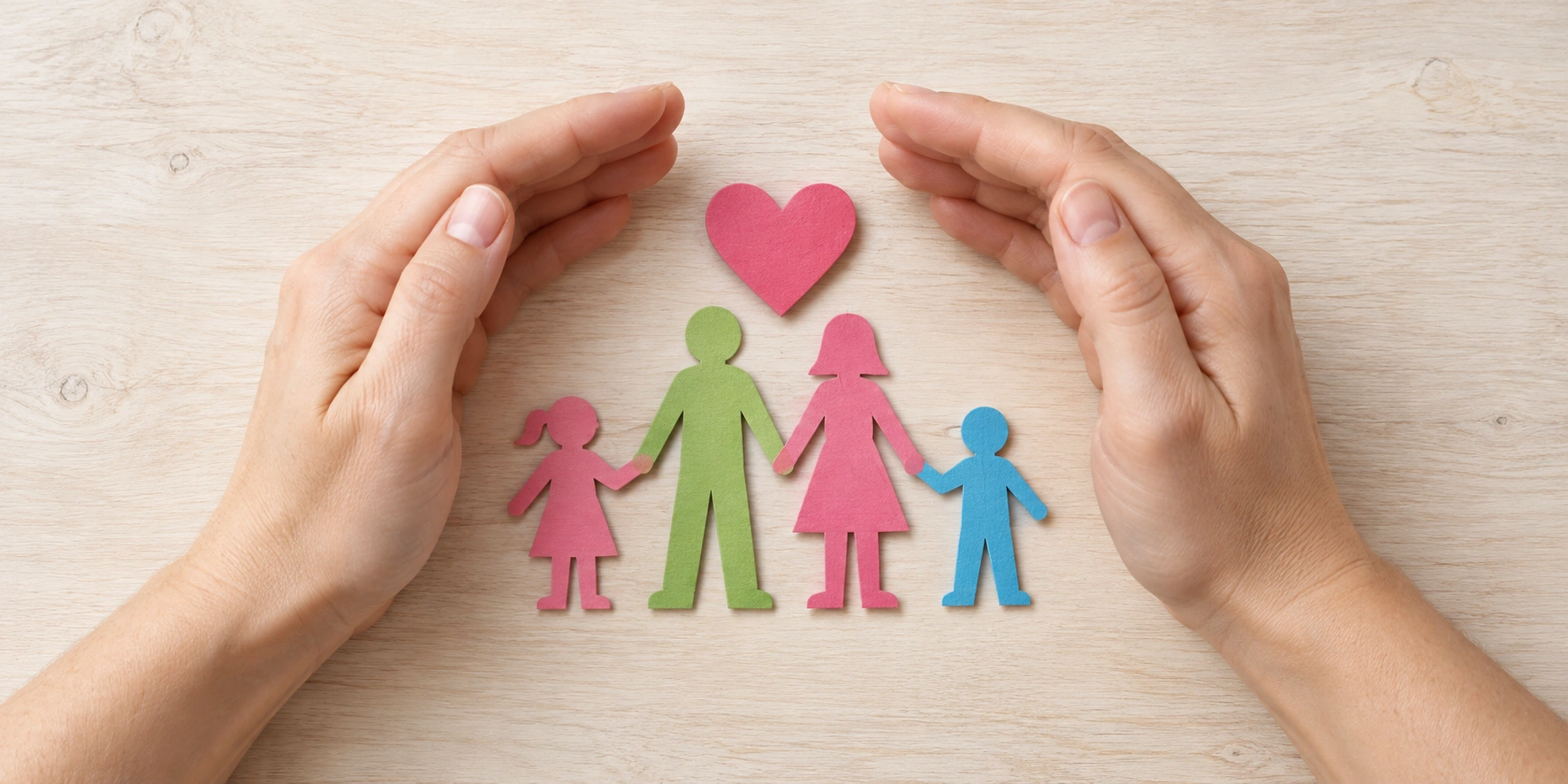 Unas manos protegen figuras de una familia de papel con un corazón rosa